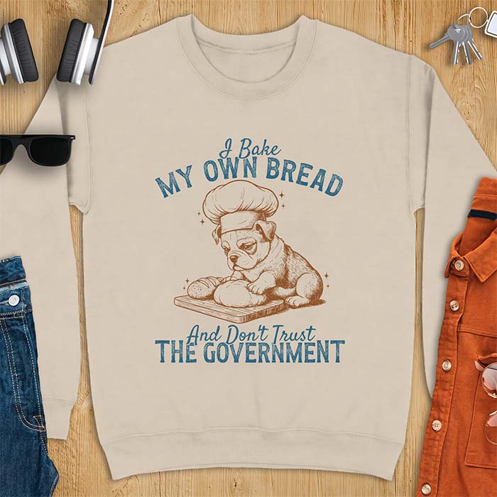 Sand sweatshirt with a graphic of a bulldog wearing a chef hat kneading bread dough on a cutting board and the text I Bake My Own Bread And Don't Trust The Government