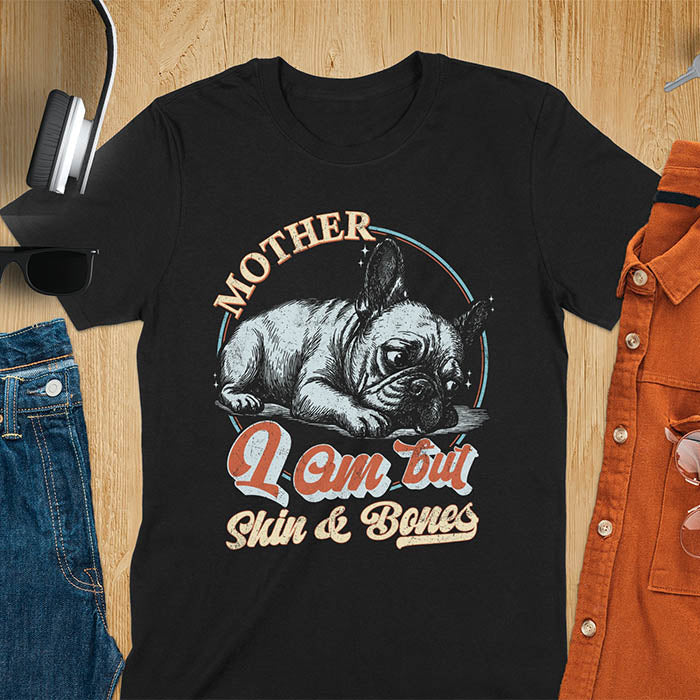 French Bulldog lying down with a sulky expression, with the text Mother I Am But Skin and Bones in retro typography on a black t-shirt