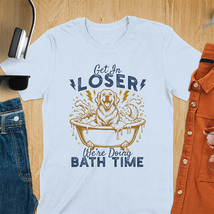 Golden Retriever sitting in a bathtub with soap bubbles and lightning bolts, with the text Get In Loser We're Doing Bath Time on a light blue t-shirt