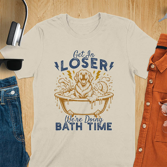 Golden Retriever sitting in a bathtub with soap bubbles and lightning bolts, with the text Get In Loser We're Doing Bath Time on a sand color t-shirt
