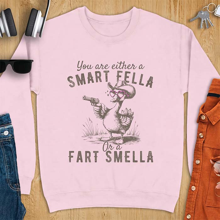 Light Pink sweatshirt with a cowboy goose illustration wearing a hat and pink heart shaped sunglasses, holding a revolver, and the text You Are Either A Smart Fella Or A Fart Smella