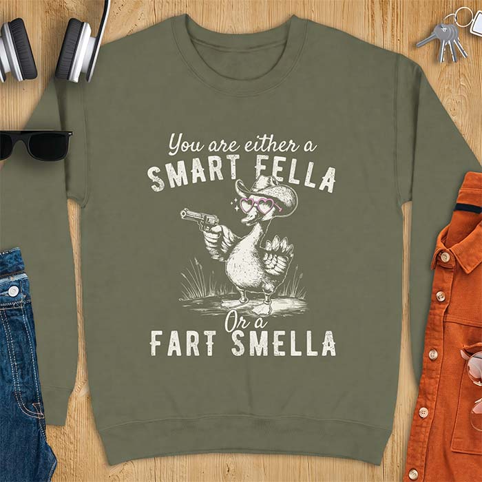 Military Green sweatshirt with a cowboy goose illustration wearing a hat and pink heart shaped sunglasses, holding a revolver, and the text You Are Either A Smart Fella Or A Fart Smella