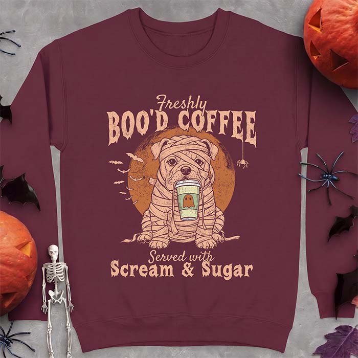 Maroon sweatshirt with a Halloween graphic of a bulldog wrapped as a mummy holding a coffee cup, bats and a spider under a moon and the text Freshly Boo'd Coffee served with scream & sugar
