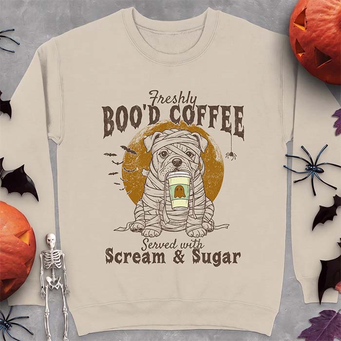 Sand sweatshirt with a Halloween graphic of a bulldog wrapped as a mummy holding a coffee cup, bats and a spider under a moon and the text Freshly Boo'd Coffee served with scream & sugar