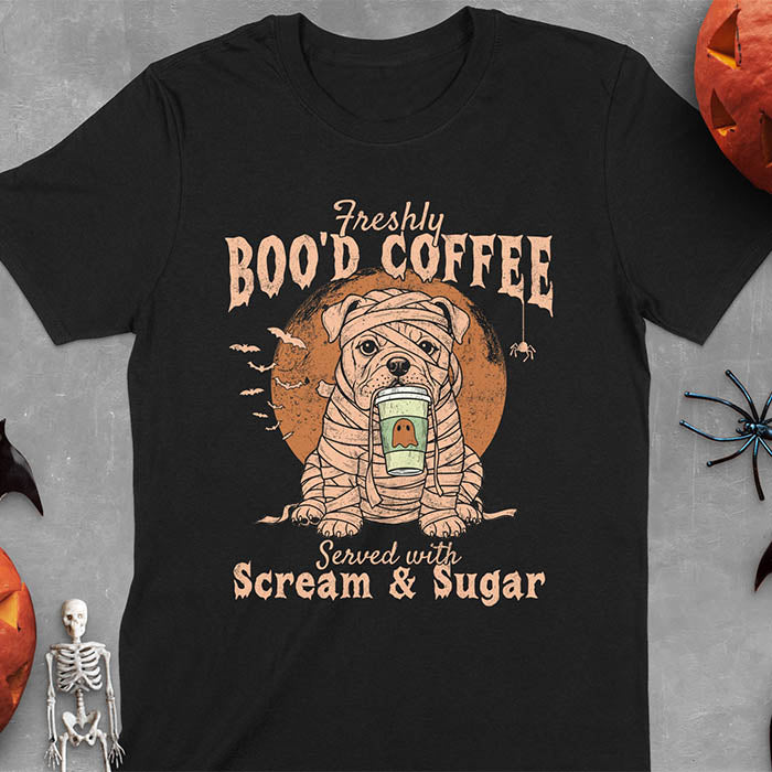 Black t-shirt featuring a mummy-wrapped bulldog holding a coffee cup with text 'Freshly BOO'D COFFEE Served with Scream & Sugar' with bats flying in background, full moon behind the bulldog, and a spider hanging from the coffee text