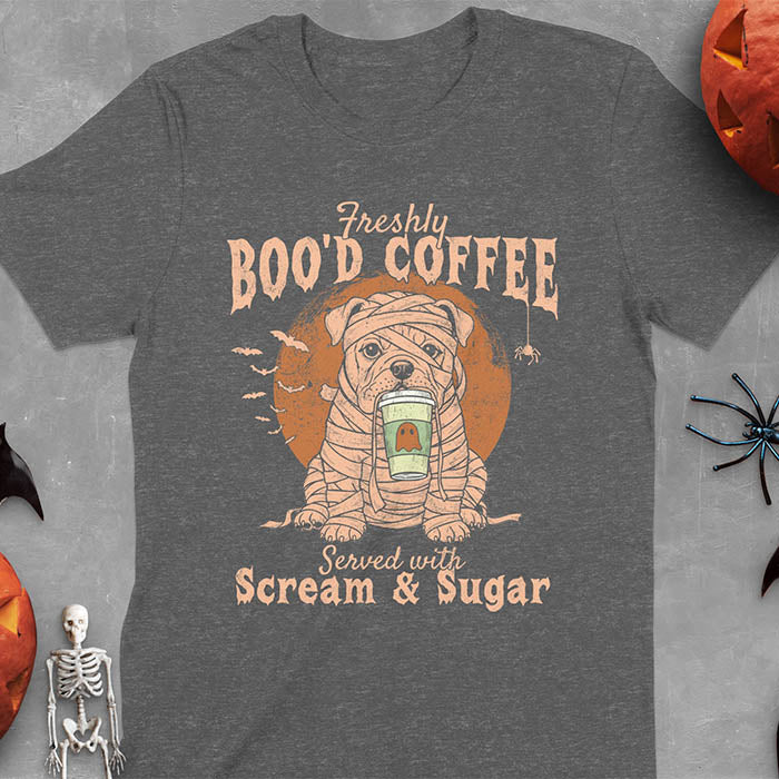 Dark heather t-shirt featuring a mummy-wrapped bulldog holding a coffee cup with text 'Freshly BOO'D COFFEE Served with Scream & Sugar' with bats flying in background, full moon behind the bulldog, and a spider hanging from the coffee text