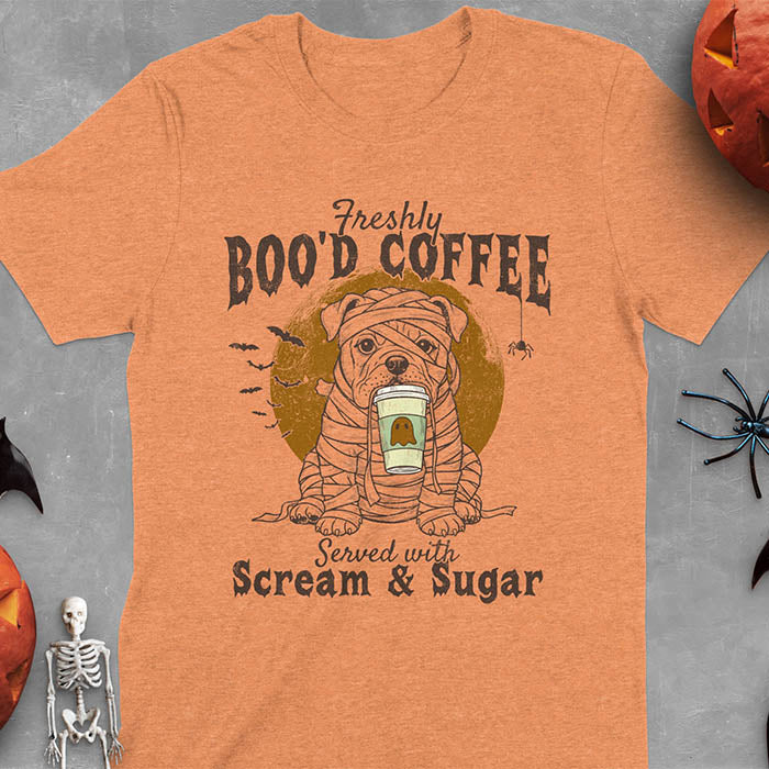 Heather Orange t-shirt featuring a mummy-wrapped bulldog holding a coffee cup with text 'Freshly BOO'D COFFEE Served with Scream & Sugar' with bats flying in background, full moon behind the bulldog, and a spider hanging from the coffee text