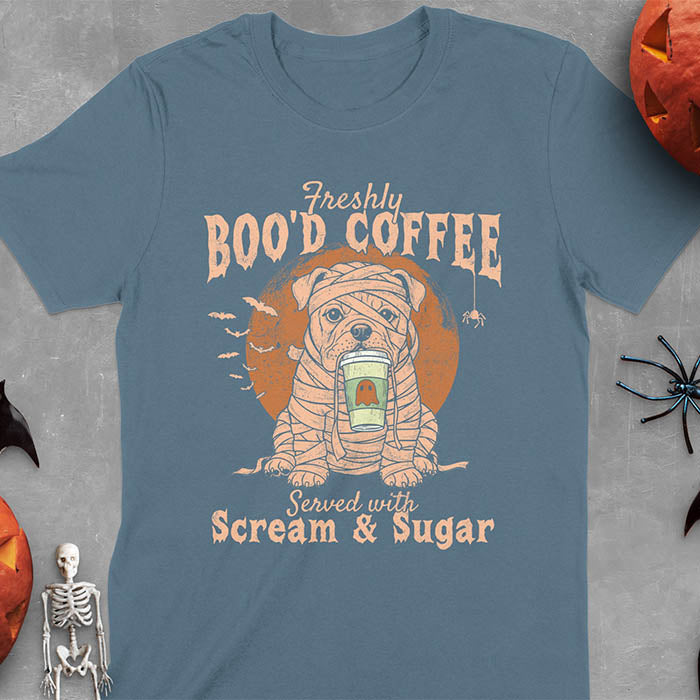 Indigo Blue t-shirt featuring a mummy-wrapped bulldog holding a coffee cup with text 'Freshly BOO'D COFFEE Served with Scream & Sugar' with bats flying in background, full moon behind the bulldog, and a spider hanging from the coffee text