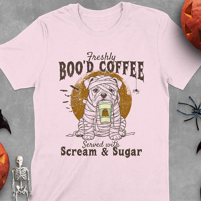 Light Pink t-shirt featuring a mummy-wrapped bulldog holding a coffee cup with text 'Freshly BOO'D COFFEE Served with Scream & Sugar' with bats flying in background, full moon behind the bulldog, and a spider hanging from the coffee text