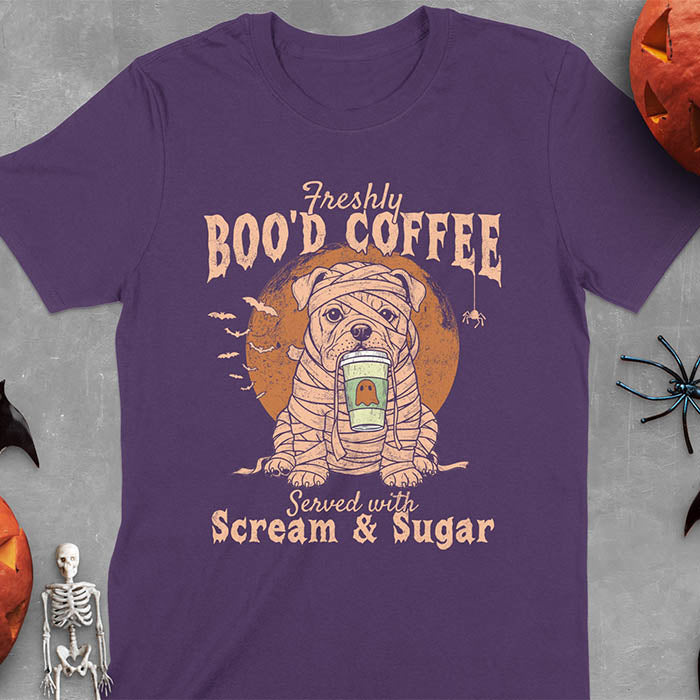 Purple t-shirt featuring a mummy-wrapped bulldog holding a coffee cup with text 'Freshly BOO'D COFFEE Served with Scream & Sugar' with bats flying in background, full moon behind the bulldog, and a spider hanging from the coffee text