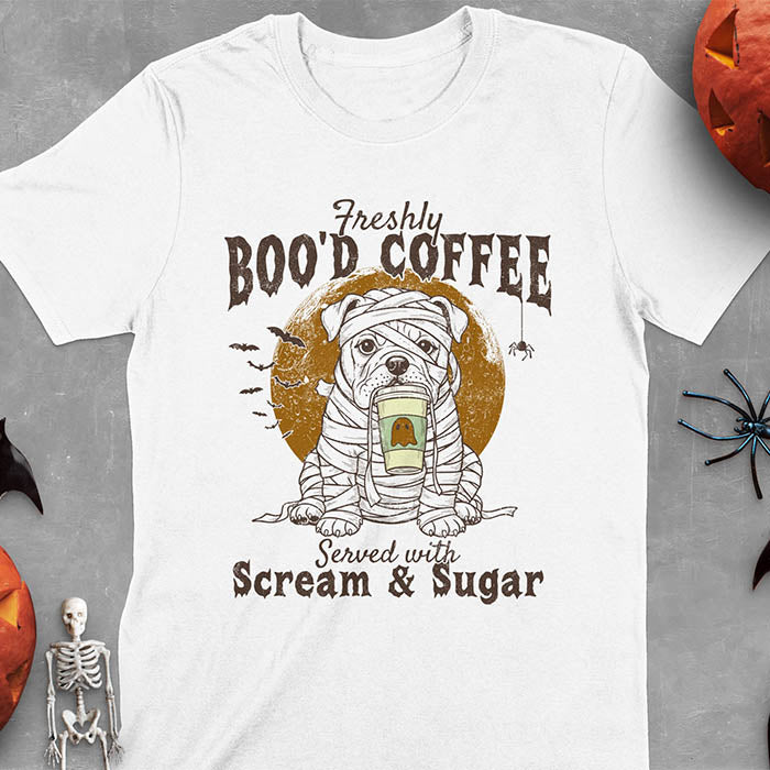 White t-shirt featuring a mummy-wrapped bulldog holding a coffee cup with text 'Freshly BOO'D COFFEE Served with Scream & Sugar' with bats flying in background, full moon behind the bulldog, and a spider hanging from the coffee text