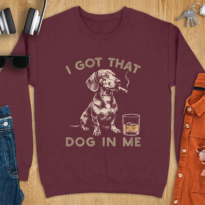 Maroon sweatshirt with a graphic of a dachshund sitting with a cigar in its mouth and a glass of whiskey beside it and the text I Got That Dog In Me