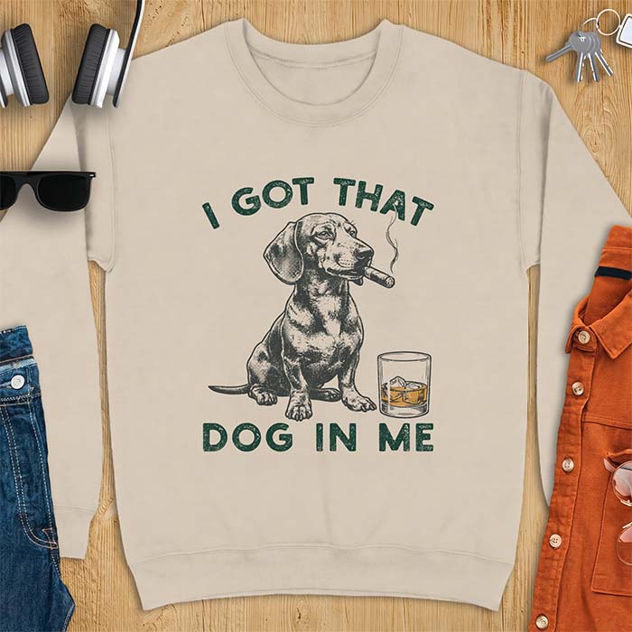 Sand sweatshirt with a graphic of a dachshund sitting with a cigar in its mouth and a glass of whiskey beside it and the text I Got That Dog In Me