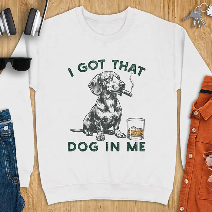 White sweatshirt with a graphic of a dachshund sitting with a cigar in its mouth and a glass of whiskey beside it and the text I Got That Dog In Me