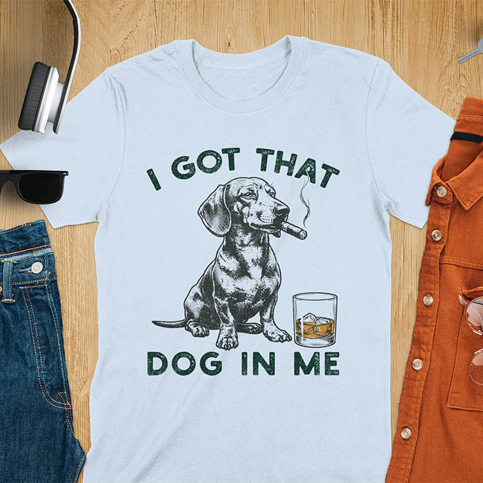 Light blue t-shirt with a vintage graphic of a dachshund smoking a cigar next to a whisky glass, with the text I Got That Dog In Me