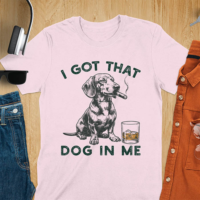 Light pink t-shirt with a vintage graphic of a dachshund smoking a cigar next to a whisky glass, with the text I Got That Dog In Me