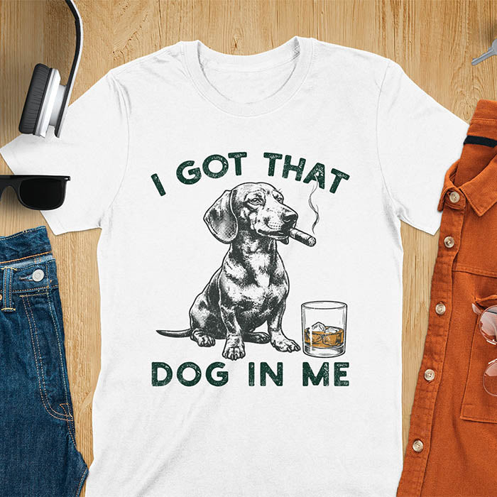 White t-shirt with a vintage graphic of a dachshund smoking a cigar next to a whisky glass, with the text I Got That Dog In Me