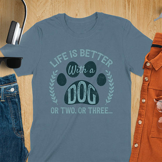 Indigo blue t-shirt featuring large paw print with text inside surrounded by laurel wreath, text reads Life Is Better With A Dog Or Two Or Three