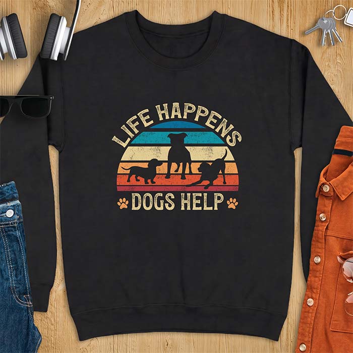 Black sweatshirt with a retro striped sunset graphic of three dog silhouettes trotting together and paw prints on either side and the text Life Happens Dogs Help