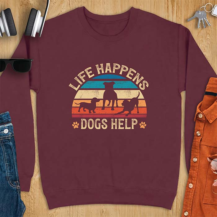 Maroon sweatshirt with a retro striped sunset graphic of three dog silhouettes trotting together and paw prints on either side and the text Life Happens Dogs Help