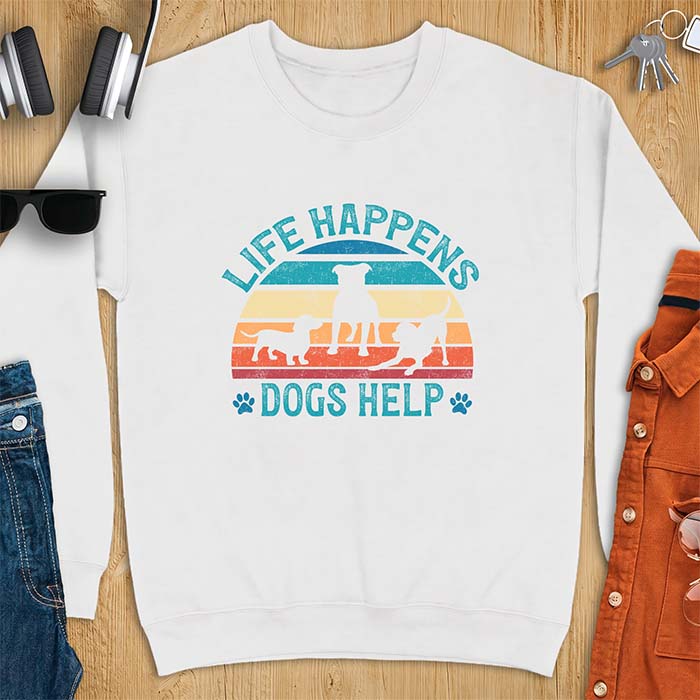 White sweatshirt with a retro striped sunset graphic of three dog silhouettes trotting together and paw prints on either side and the text Life Happens Dogs Help