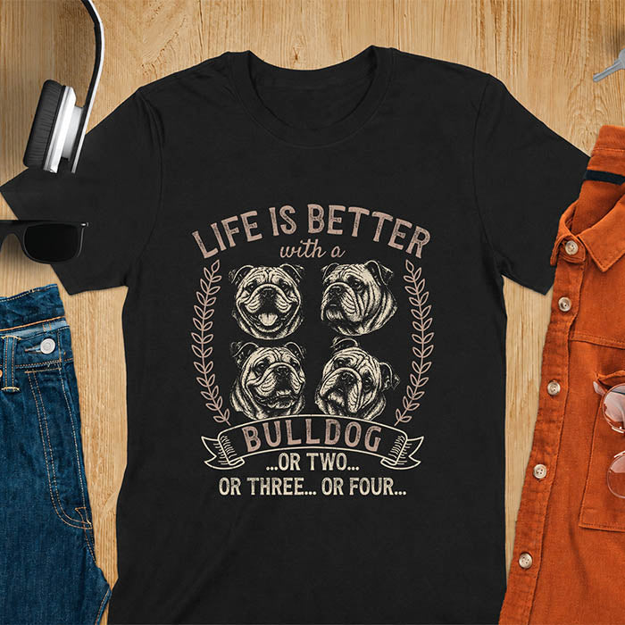 Black unisex t-shirt with distressed vintage graphic featuring four Bulldog portrait illustrations in a two-by-two grid framed by laurel branches, text reads Life Is Better with a Bulldog or two or three or four