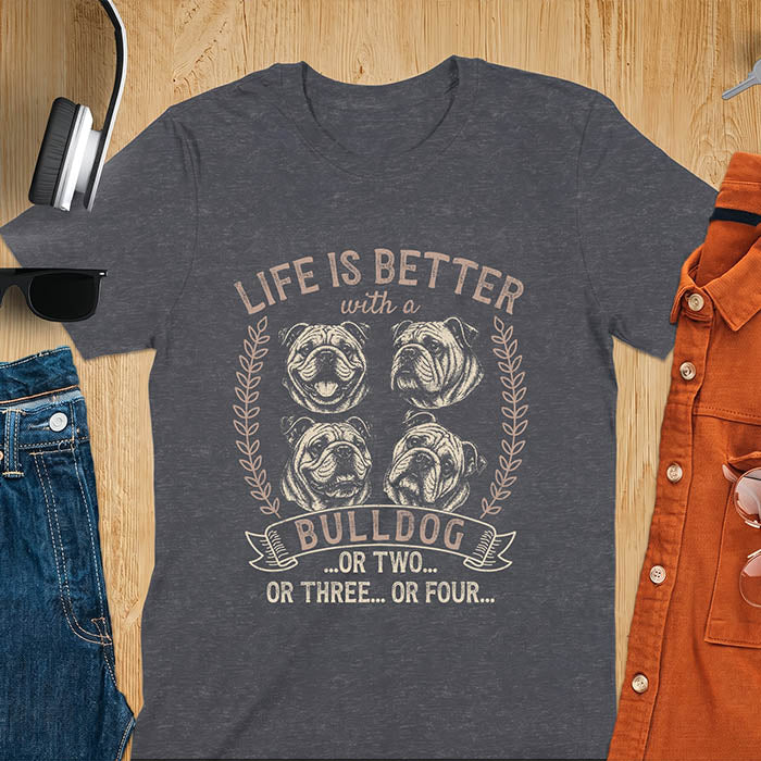 A dark heather unisex t-shirt with distressed vintage graphic featuring four Bulldog portrait illustrations in a two-by-two grid framed by laurel branches, text reads Life Is Better with a Bulldog or two or three or four