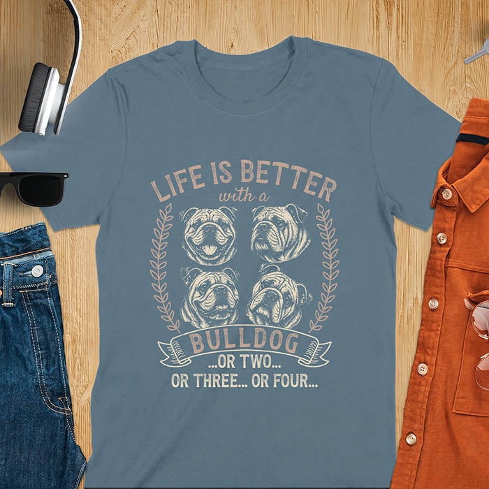 Indigo blue unisex t-shirt with distressed vintage graphic featuring four Bulldog portrait illustrations in a two-by-two grid framed by laurel branches, text reads Life Is Better with a Bulldog or two or three or four