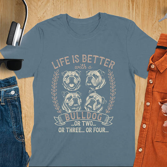Indigo blue unisex t-shirt with distressed vintage graphic featuring four Bulldog portrait illustrations in a two-by-two grid framed by laurel branches, text reads Life Is Better with a Bulldog or two or three or four