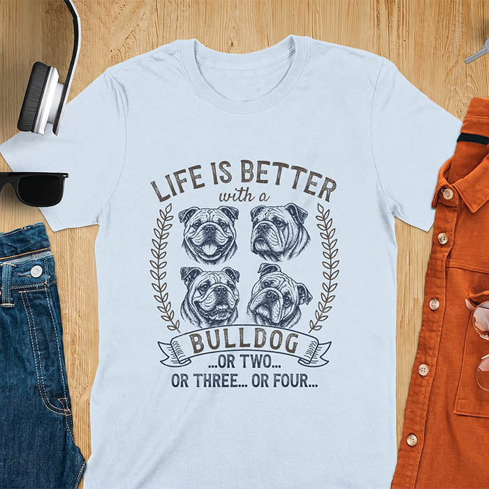 Light Blue unisex t-shirt with distressed vintage graphic featuring four Bulldog portrait illustrations in a two-by-two grid framed by laurel branches, text reads Life Is Better with a Bulldog or two or three or four
