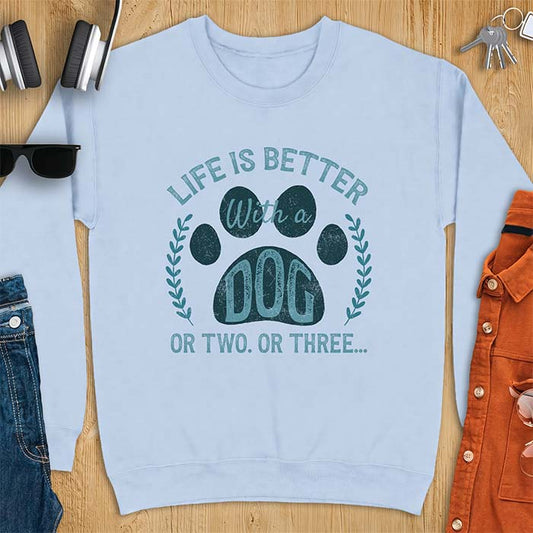 Light Blue sweatshirt with a graphic of a large paw print framed by a laurel wreath on either side and the text Life Is Better With a Dog Or Two Or Three