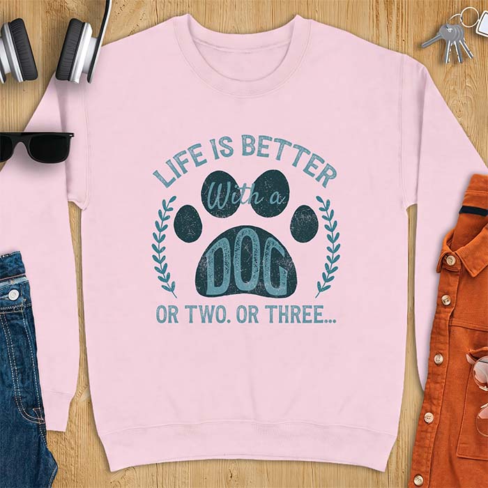 Light Pink sweatshirt with a graphic of a large paw print framed by a laurel wreath on either side and the text Life Is Better With a Dog Or Two Or Three