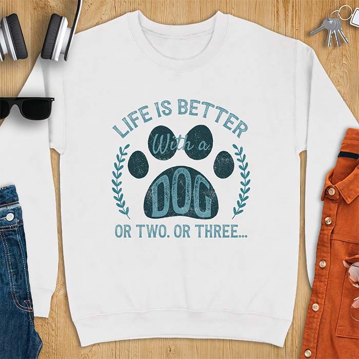 White sweatshirt with a graphic of a large paw print framed by a laurel wreath on either side and the text Life Is Better With a Dog Or Two Or Three