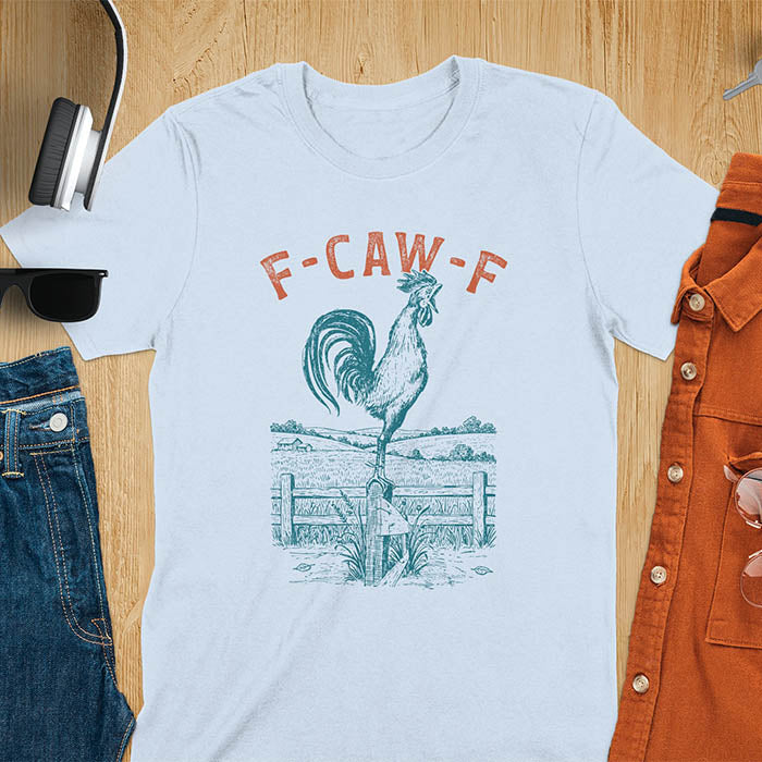 Light blue t-shirt with F-CAW-F text and detailed rooster illustration standing on wooden fence in vintage farm scene style
