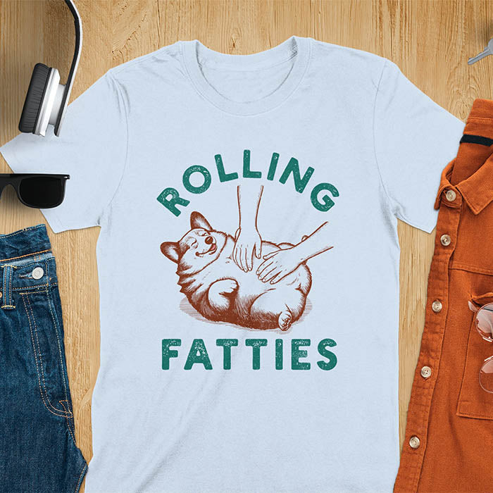 Chubby corgi illustration enjoying tummy rubs with Rolling Fatties text in textured lettering on light blue tee