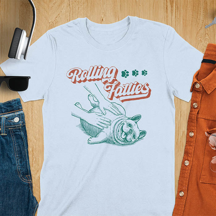 Light blue t-shirt with Rolling Fatties script text and French Bulldog being petted by human hands in line drawing style.