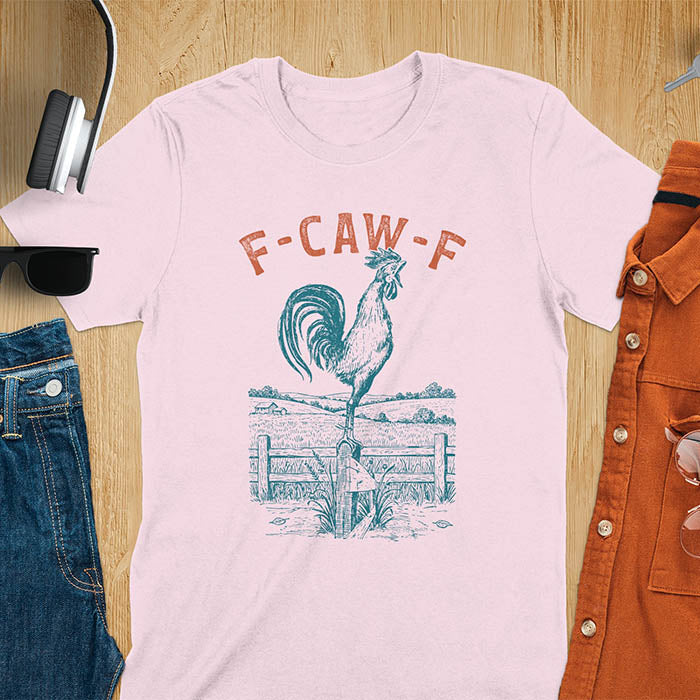 Light pink t-shirt with F-CAW-F text and detailed rooster illustration standing on wooden fence in vintage farm scene style