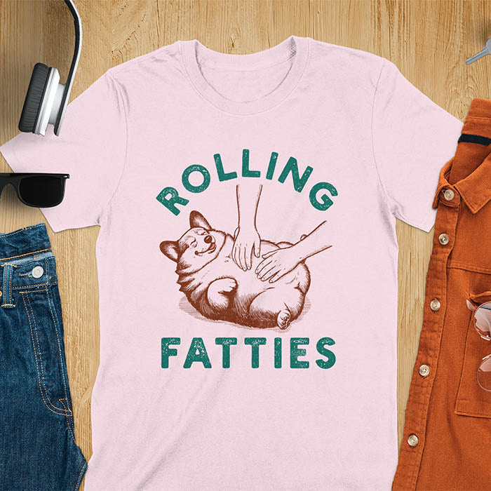Chubby corgi illustration enjoying tummy rubs with Rolling Fatties text in textured lettering on light pink tee