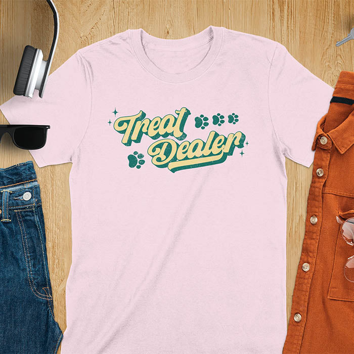 Light pink t-shirt with Treat Dealer text in retro script typography with green and yellow colors and paw print decorations