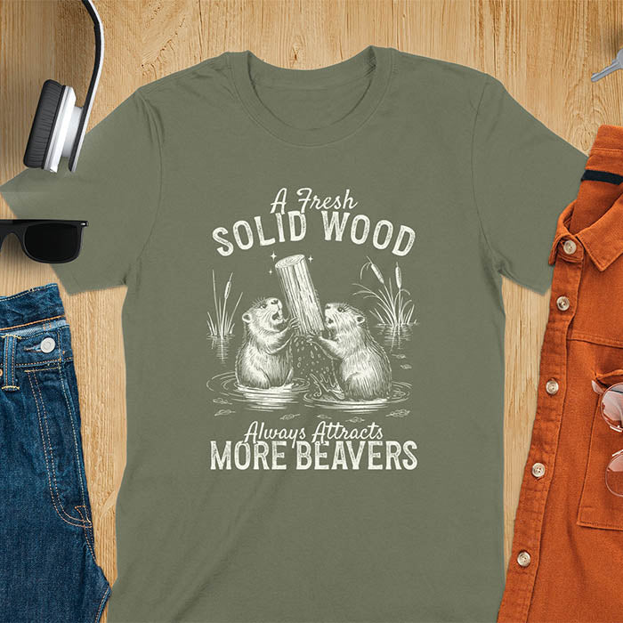 Military Green Light blue t-shirt with vintage-style illustration of two beavers in water fighting over a wooden log, featuring text 'A Fresh Solid Wood Always Attracts More Beavers' in rustic lettering 