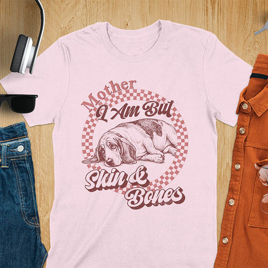 Light pink t-shirt with a vintage graphic of a basset hound lying down inside a retro checkered circle, with the text Mother I Am But Skin and Bones