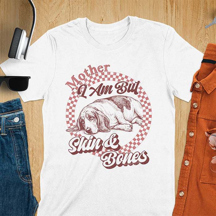 White t-shirt with a vintage graphic of a basset hound lying down inside a retro checkered circle, with the text Mother I Am But Skin and Bones