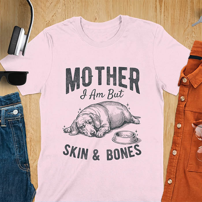 Light pink graphic tee with vintage sketch of a chonky sausage dog lying next to an empty bowl, text reads Mother I Am But Skin And Bones