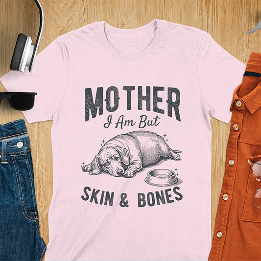 Light pink graphic tee with vintage sketch of a chonky sausage dog lying next to an empty bowl, text reads Mother I Am But Skin And Bones