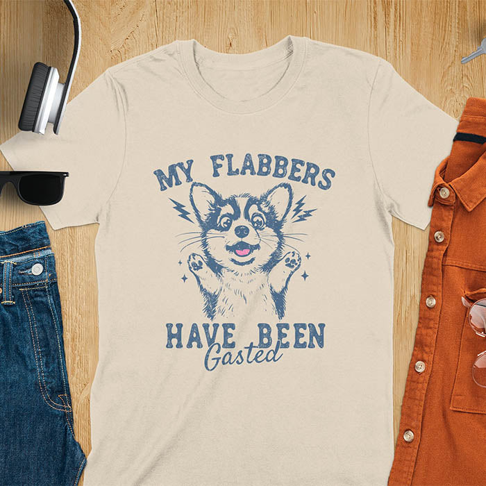 A sand color t-shirt with a bewildered corgi with its paws up. Text: MY FLABBERS above and HAVE BEEN GASTED below. This sarcastic tee-shirt features kawaiiness cuteness, a genz meme tee. A depress meme and anxiety tshirt, a funny gag gift. One of those shirts that go hard, a weirdcore memes and sad core aesthetic. A mom gift alternative.
