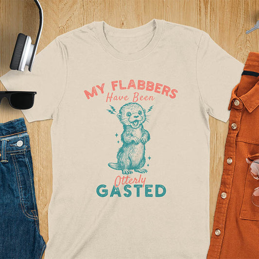 A sand color t-shirt with a startled-looking otter holding its paws in front of its chest. Sparkles surround the otter. Text: "MY FLABBERS" above and "HAVE BEEN Otterly GASTED" below. This weird silly funny tee shows Kawaiiness cuteness and Otter cuteness, a great Otter lover gift. A Sarcastic t-shirt and Funny gag gift, a Gen Z meme tee tapping into Weirdcore memes. An Animal person gift and Gift for mom, hers, one of the Shirts that go hard featuring a Cute sea otter.