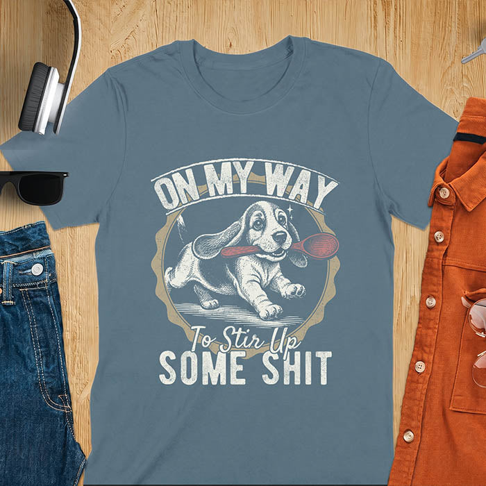 Indigo Blue graphic tee with vintage stamp illustration of a basset hound running with a wooden spoon, text reads On My Way To Stir Up Some Shit