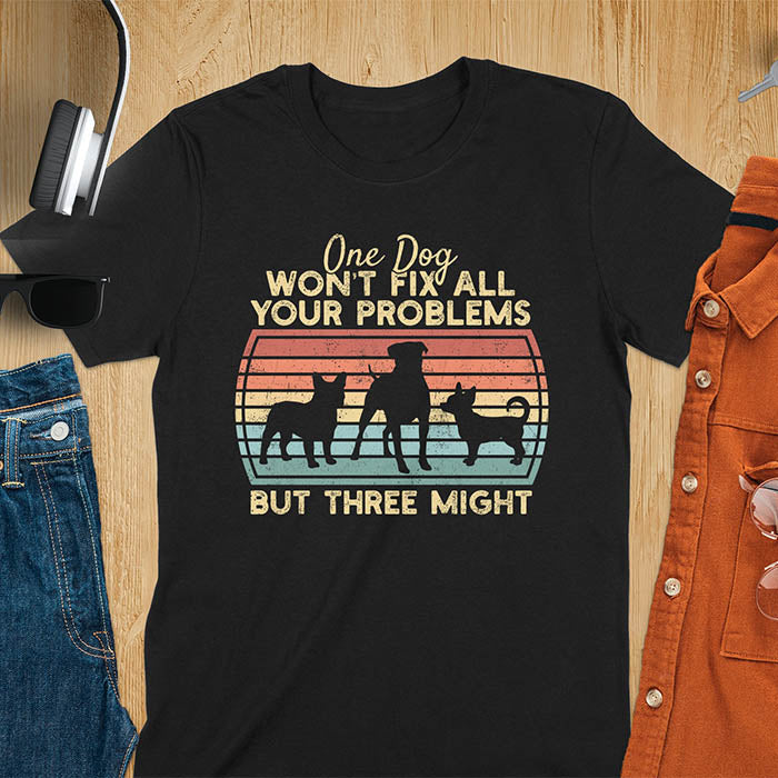 Black t-shirt with text 'One dog won't fix all your problems but three might' and three dog silhouettes on vintage sunset stripes