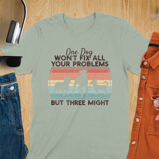 Sage green  t-shirt with text 'One dog won't fix all your problems but three might' and three dog silhouettes on vintage sunset stripes