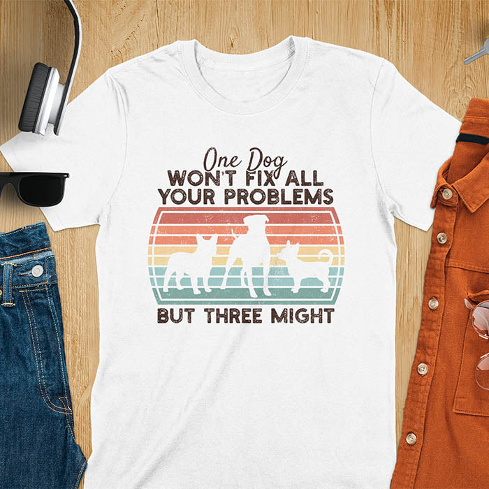 White t-shirt with text 'One dog won't fix all your problems but three might' and three dog silhouettes on vintage sunset stripes